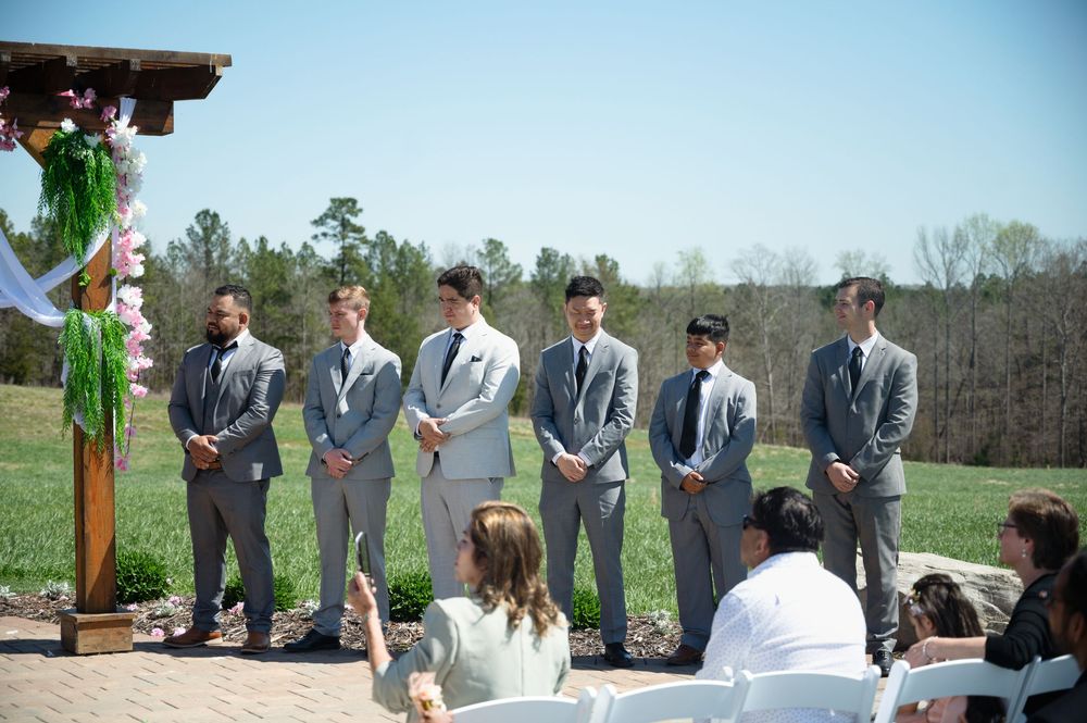 Groomsmen in matching gray suits standing at outdoor wedding ceremony altar.