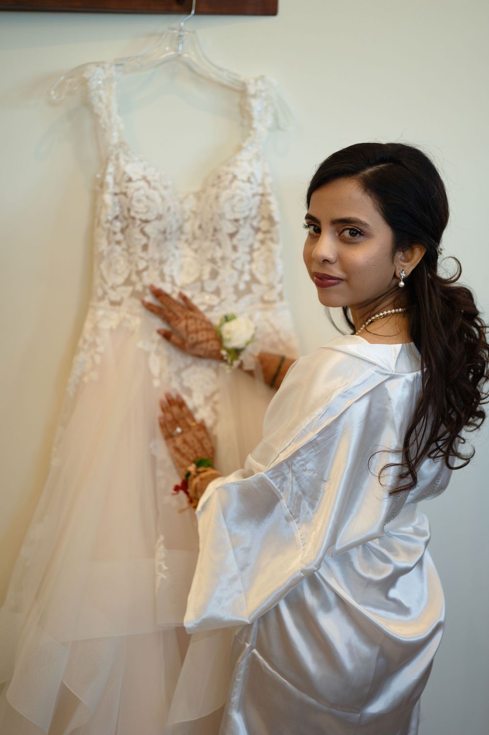 Bride in white robe with henna hands holding lace wedding dress.