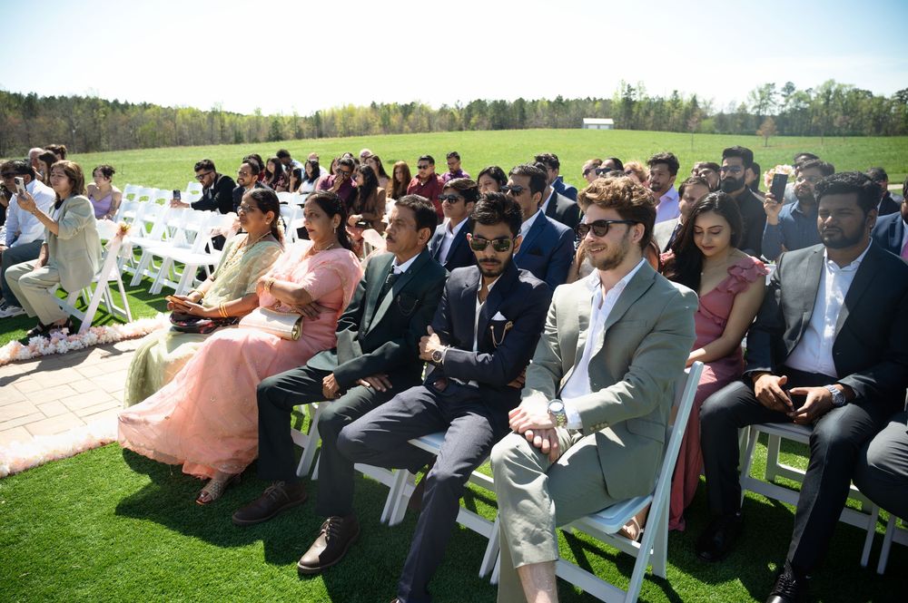 Guests seated in white chairs at an outdoor wedding ceremony on a sunny day.