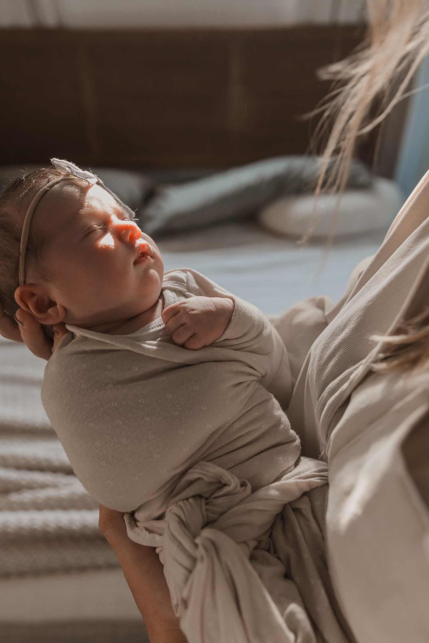 Newborn baby swaddled in beige wrap sleeping peacefully in mothers arms.