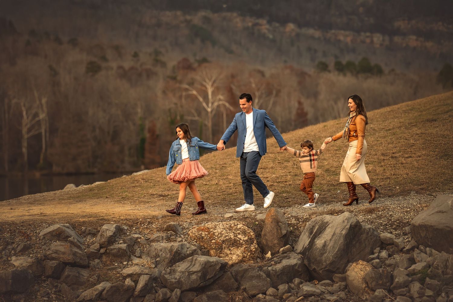 Family of 4 walking hand-in-hand on a rocky path in autumn.