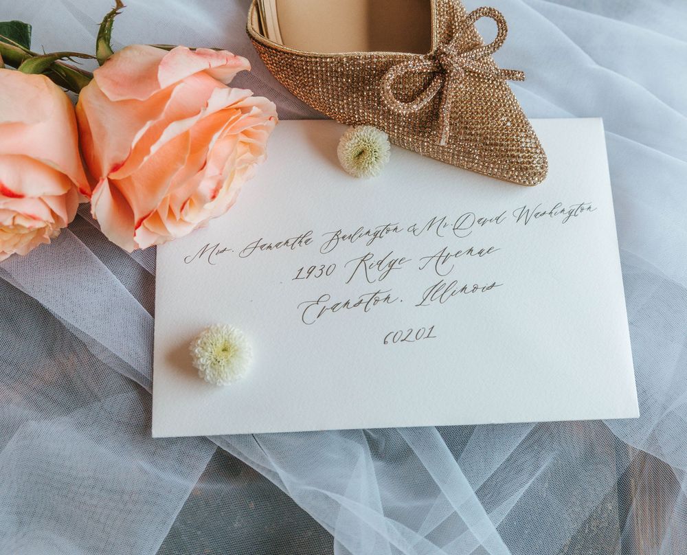 Elegant wedding envelope with gold calligraphy, peach roses, burlap bow, and white flowers on sheer tulle fabric.