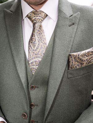 Man wearing sage green three-piece suit with gold paisley tie and matching pocket square.