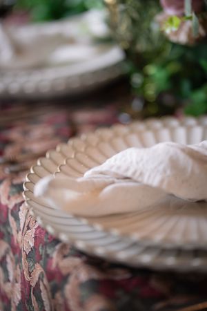 Elegant vintage glass plate with white linen napkin on floral tablecloth for a romantic wedding reception.