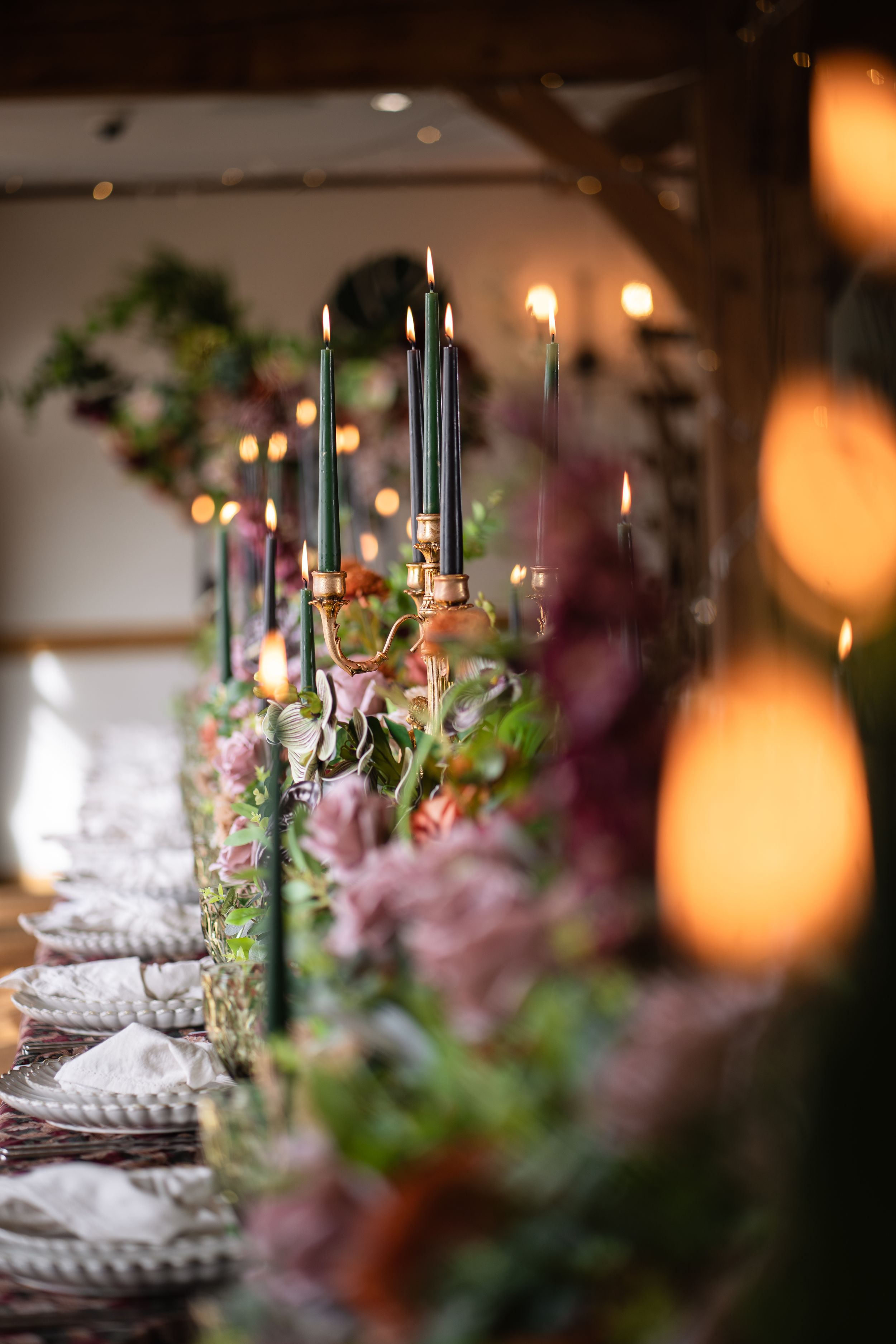 Elegant wedding table set with tall green candles, lush floral arrangements, and warm glowing lights.