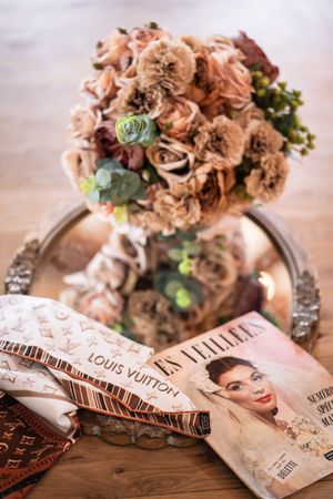 Romantic bridal bouquet of dusty pink flowers on silver tray beside Louis Vuitton ribbon and vintage magazine.