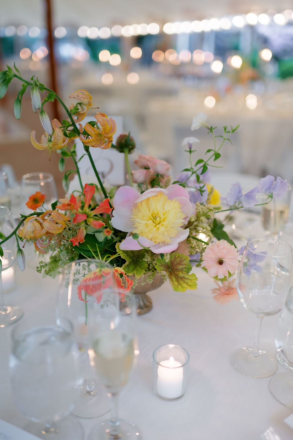 Elegant floral centerpiece with pastel blooms in a silver bowl surrounded by candles and glassware.