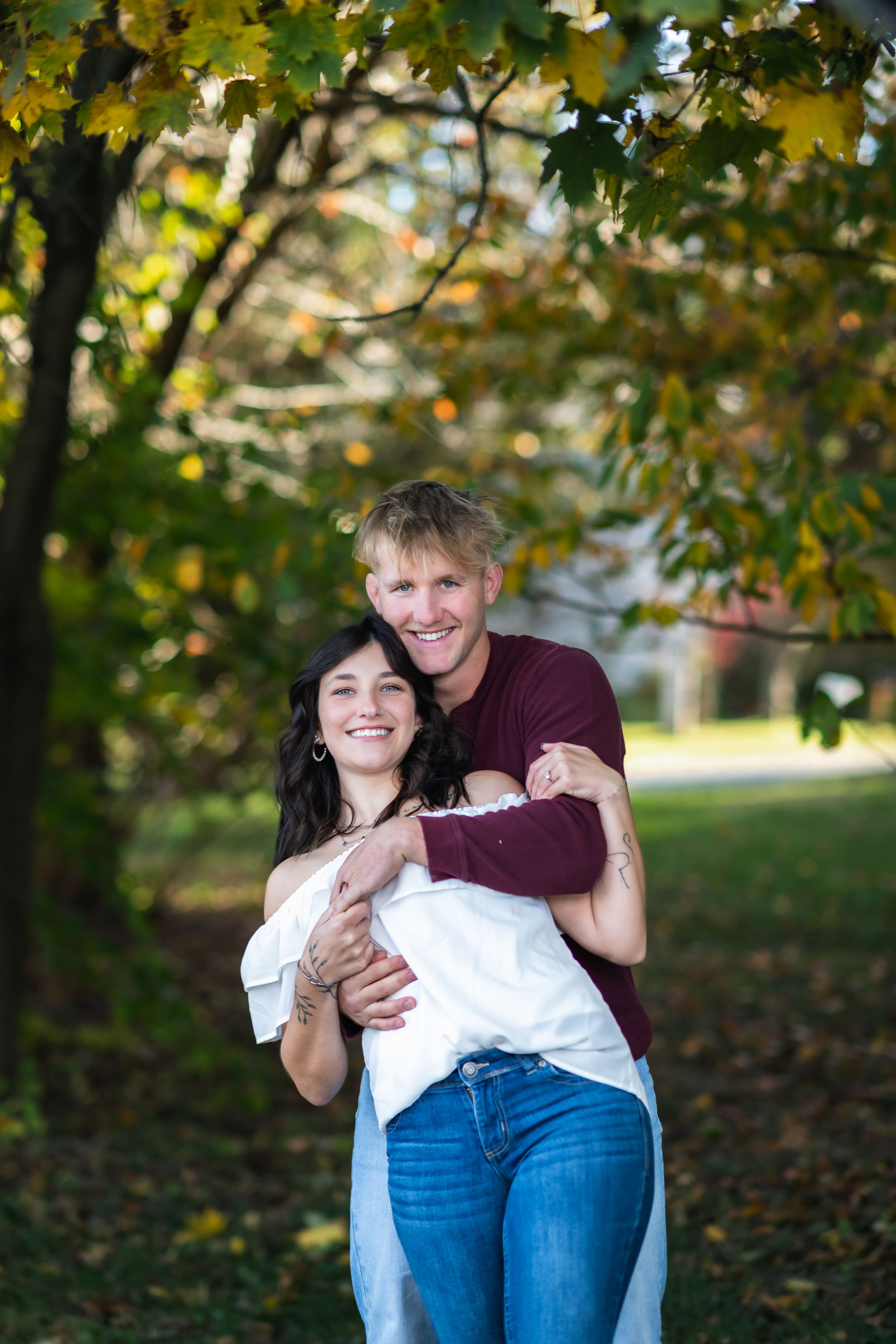 Happy couple embracing outdoors in autumn park with colorful fall foliage trees in background.