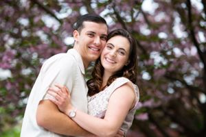 A romantic engagement photo with cherry blossoms blooming in the background.