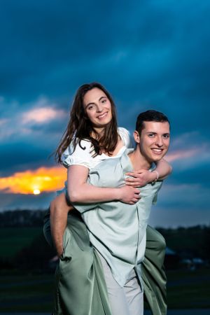 Playful piggyback portrait at sunset with dramatic blue and orange sky.
