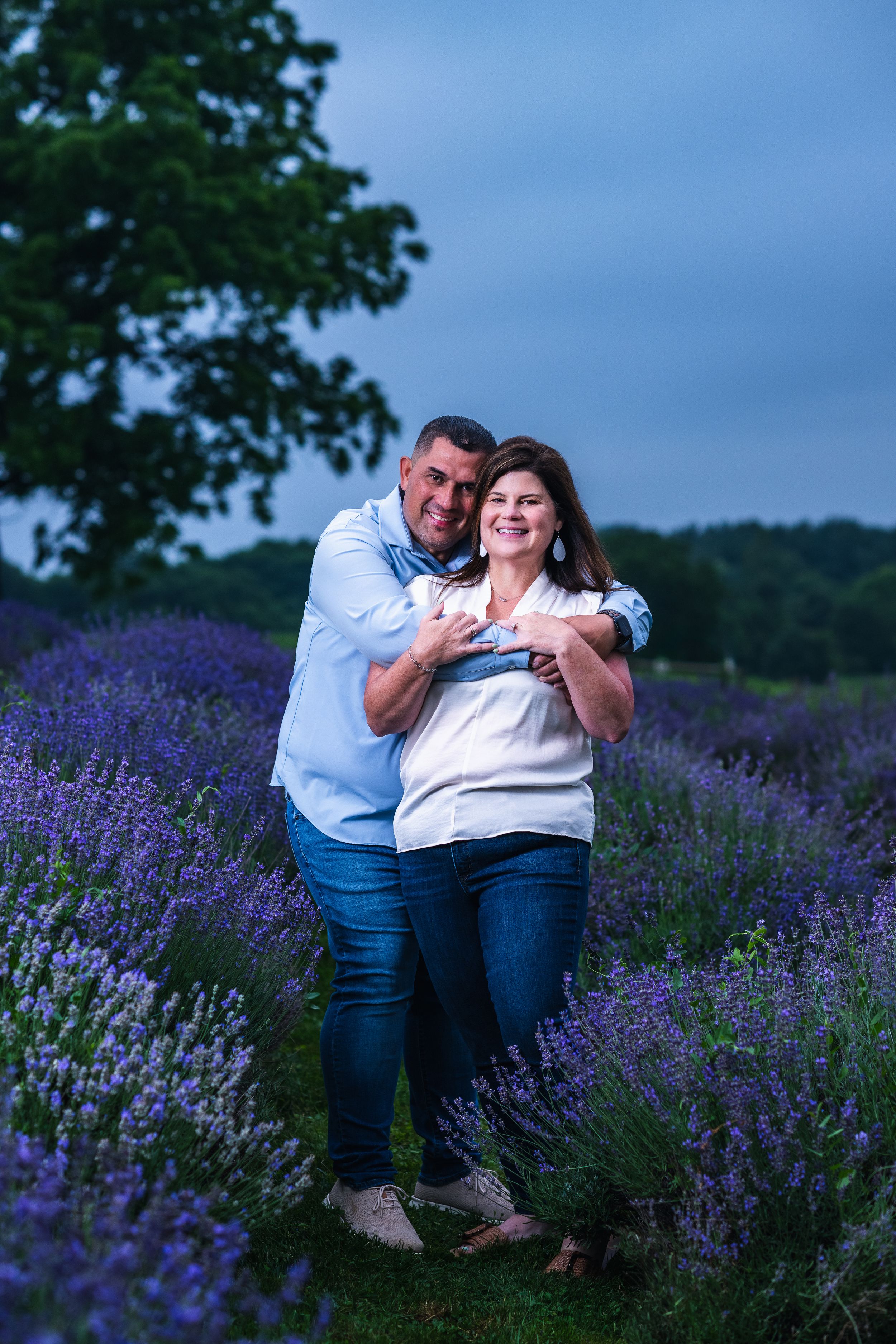 Couple embracing in a lavender field at dusk, making a heart shape with their hands, surrounded by purple blooms.