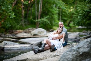 A couple sitting together on rocks by a flowing stream in a wooded setting.