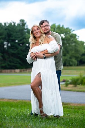 Couple posing together outdoors in white dress and casual wear on grassy field.