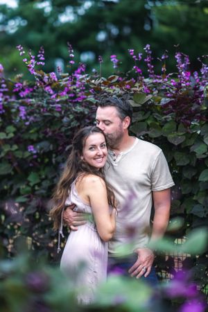 Romantic couple embracing among purple flowering plants in garden setting.