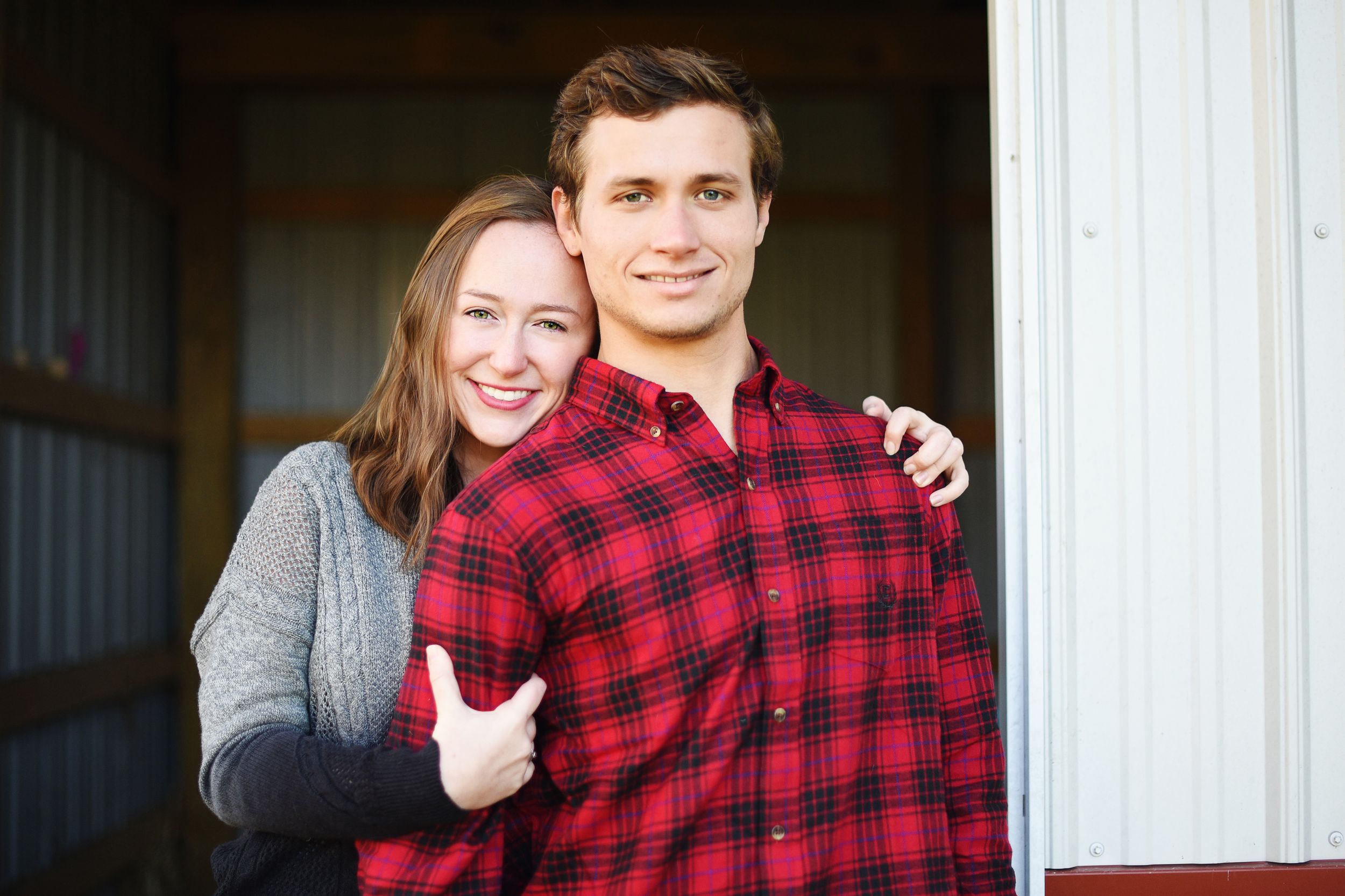 Casual couple portrait with person in plaid flannel and gray sweater by doorway.