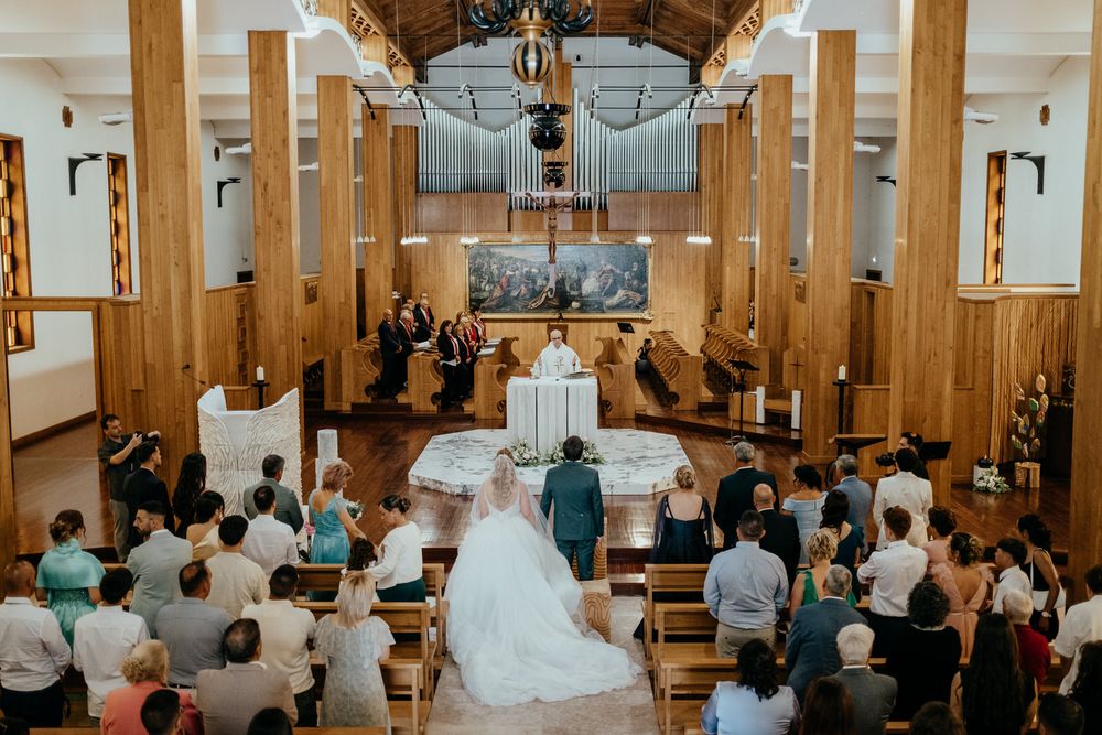 Bride and groom walk down the aisle of a wooden church filled with wedding guests during a ceremony.