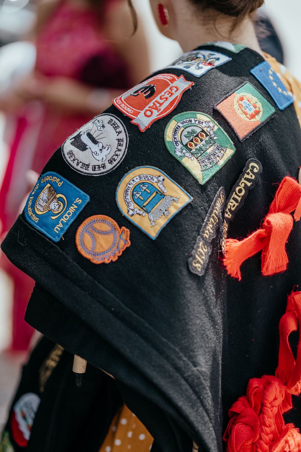 Black shawl covered in colorful embroidered patches and badges with red fringe trim worn at festival.