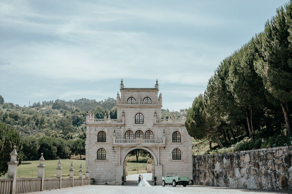 Bride and groom arrive at an elegant Italian villa archway with a vintage green car on a scenic estate.