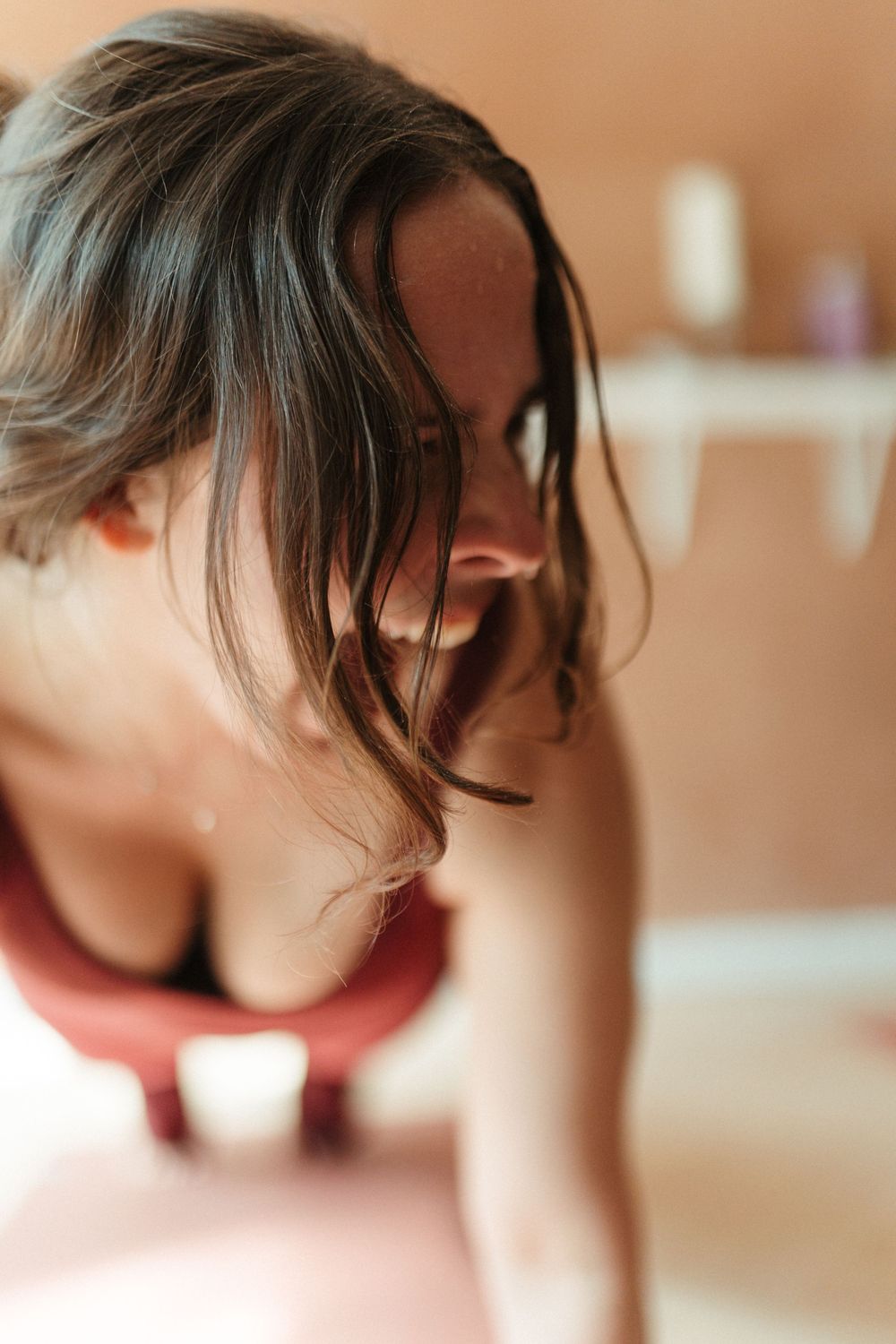 Woman with dark hair leaning forward in a yoga pose, wearing a red sports bra in a warmly lit room.