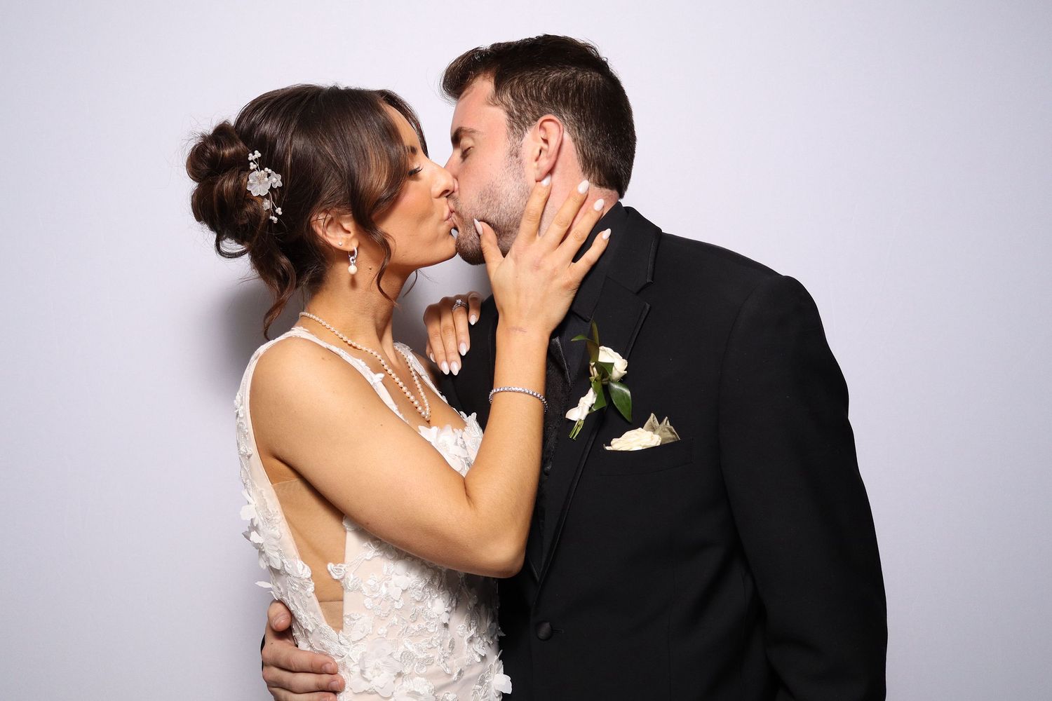 A bride and groom share a romantic kiss, dressed in wedding attire with a white floral boutonniere.