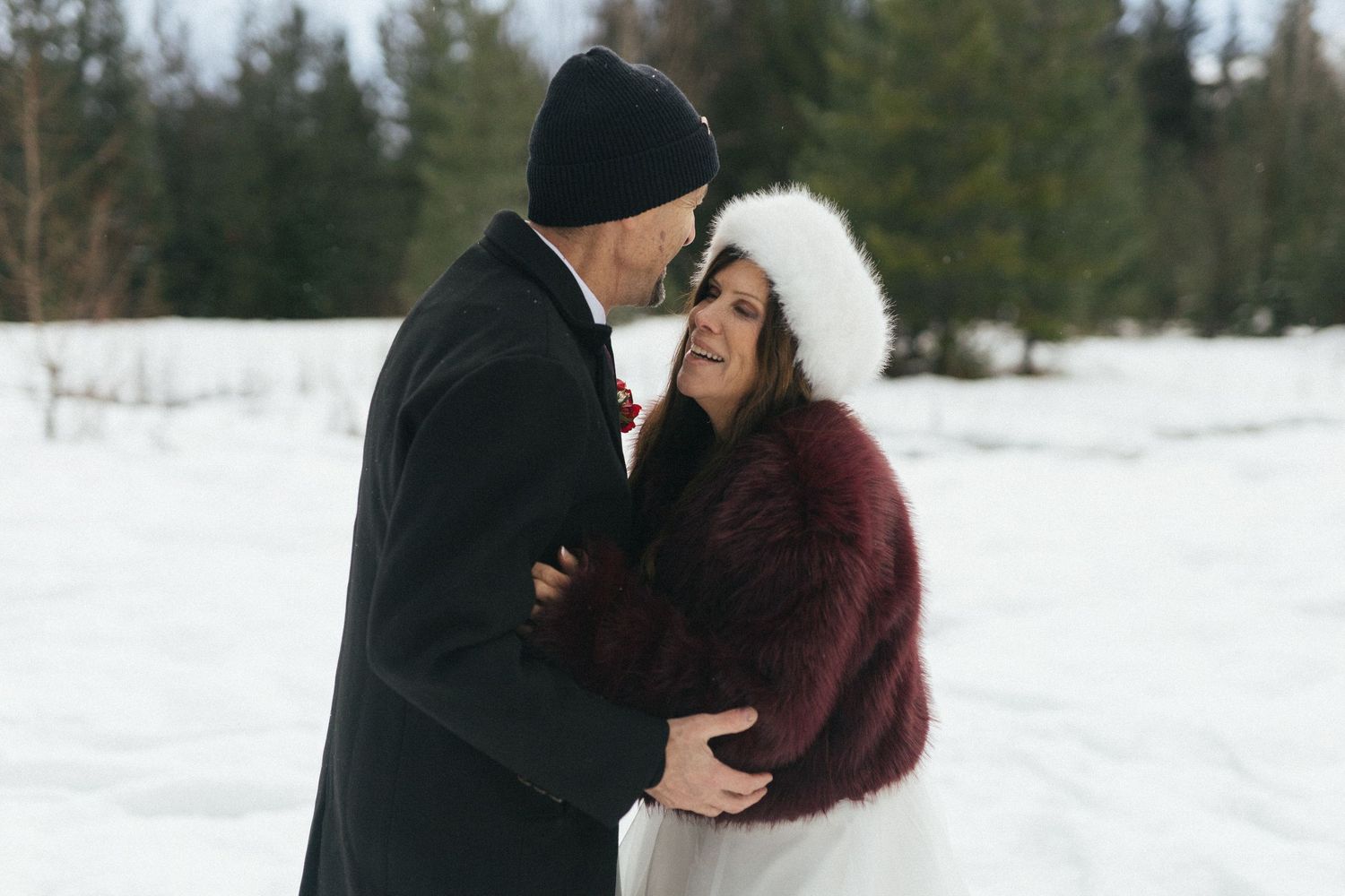 bride and groom hold each other and laugh in a snowy forest