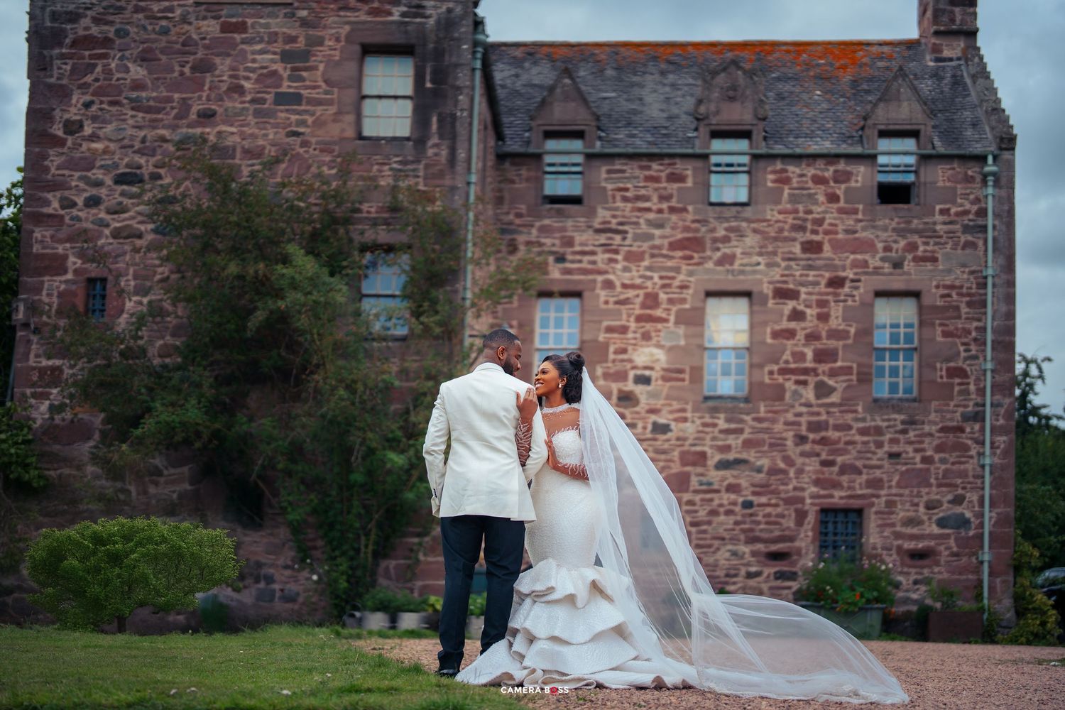 Bride and groom share a romantic moment outside a historic Scottish stone castle, bride wearing a flowing white gown with veil.