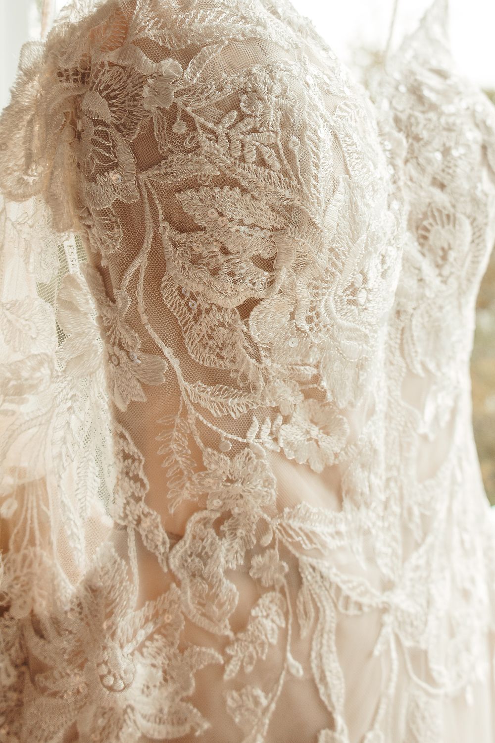 Detailed close-up of intricate floral lace pattern on elegant ivory wedding dress fabric.