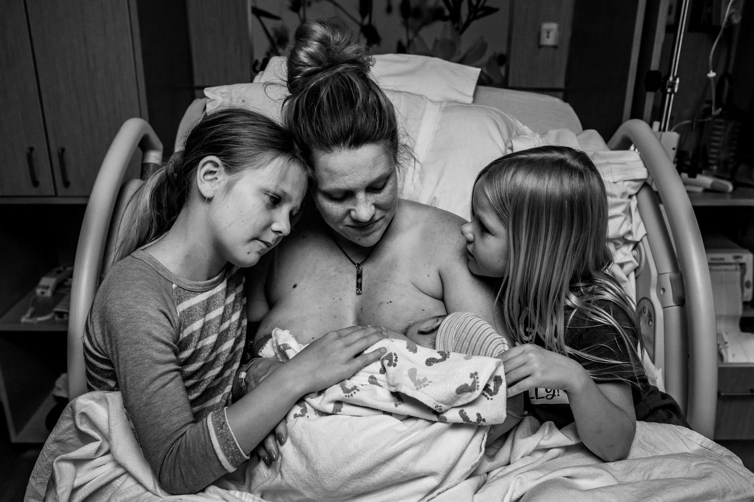 Family shares intimate moment with newborn in hospital bed.
