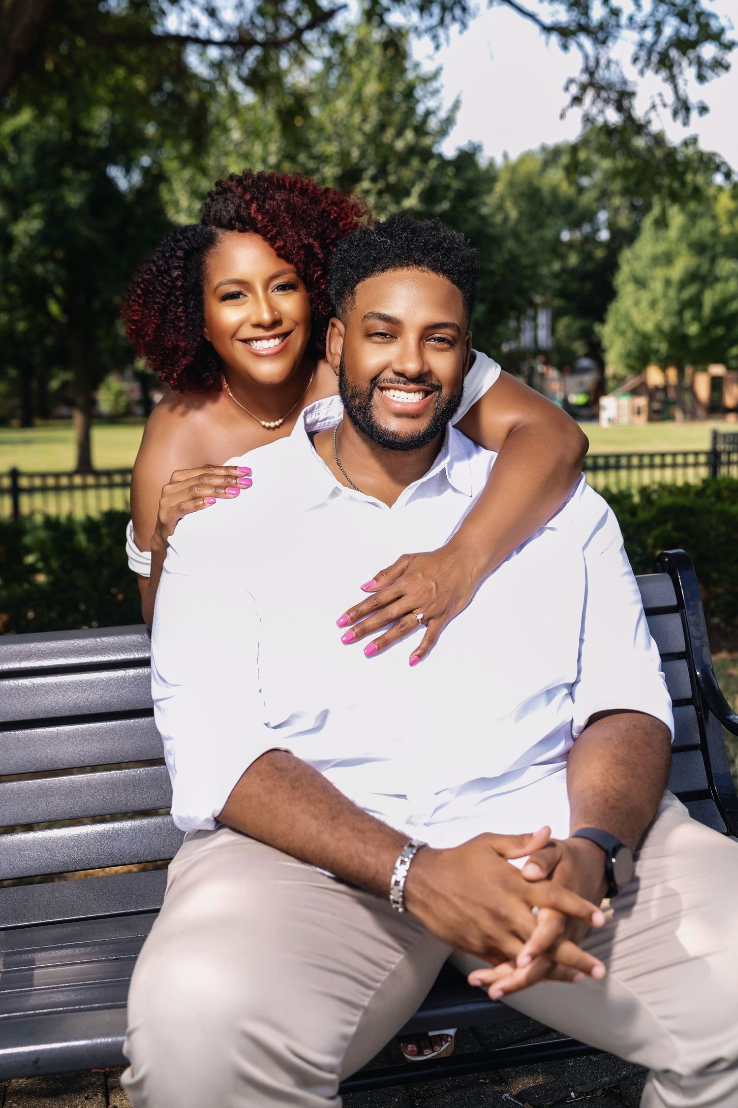 A couple sits together on a park bench sharing a tender embrace on a sunny day in a green space.