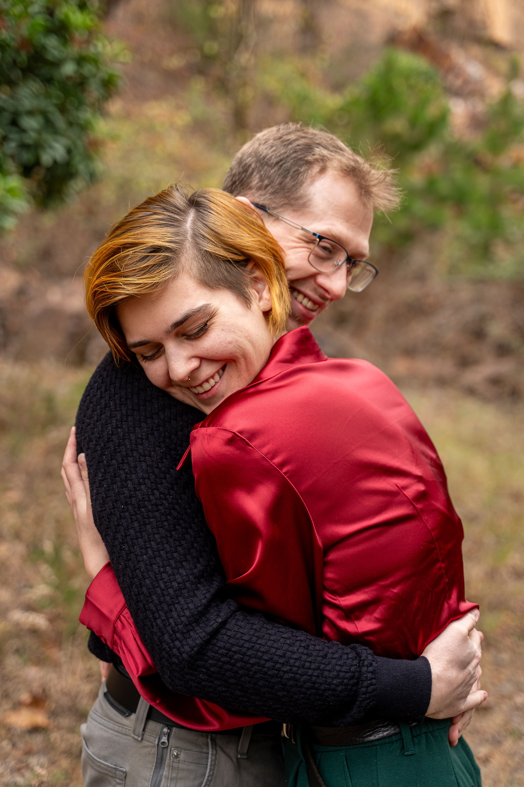 Couple hugging and smiling warmly in an outdoor natural wooded environment.