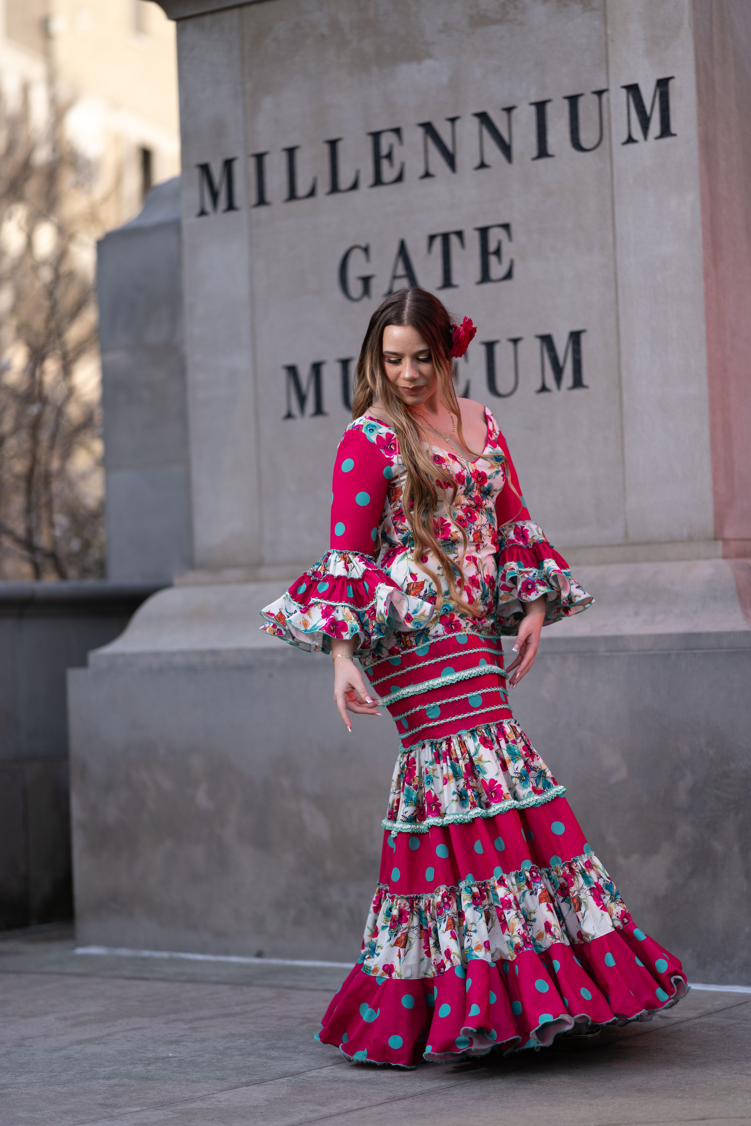 Woman in vibrant red floral flamenco dress dancing outside Millennium Gate Museum.