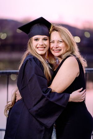 Two smiling blonde women hugging outdoors at dusk, one wearing black graduation cap and gown.