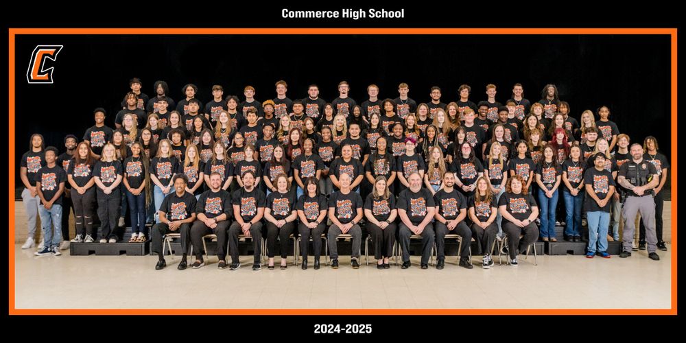 Large group panoramic photo of school marching band members in matching black uniforms seated in formal rows on risers.