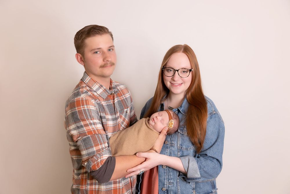 Two people wearing plaid and denim hold a small wrapped bundle against a neutral beige background.