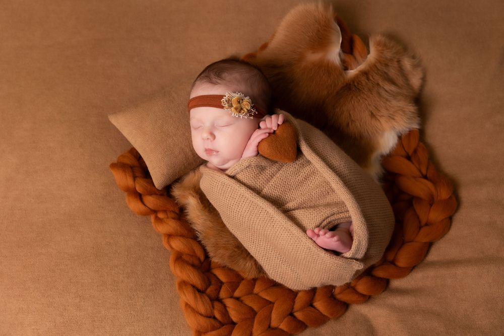 Newborn sleeping in beige wrap nestled in braided brown basket from overhead view.