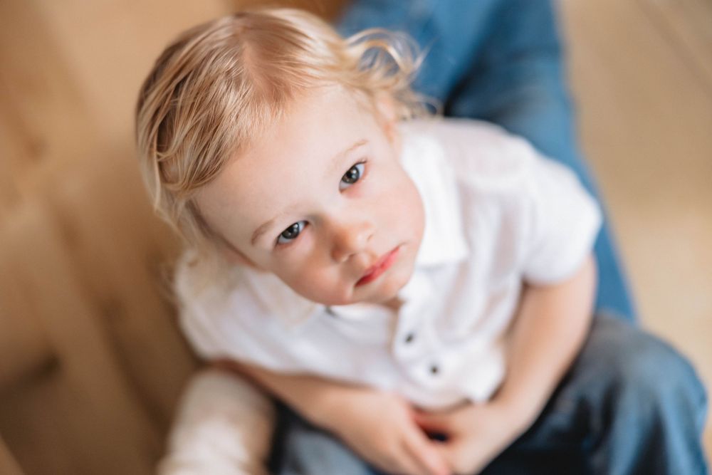 Sweet blonde toddler child in white shirt looking up with big blue eyes.
