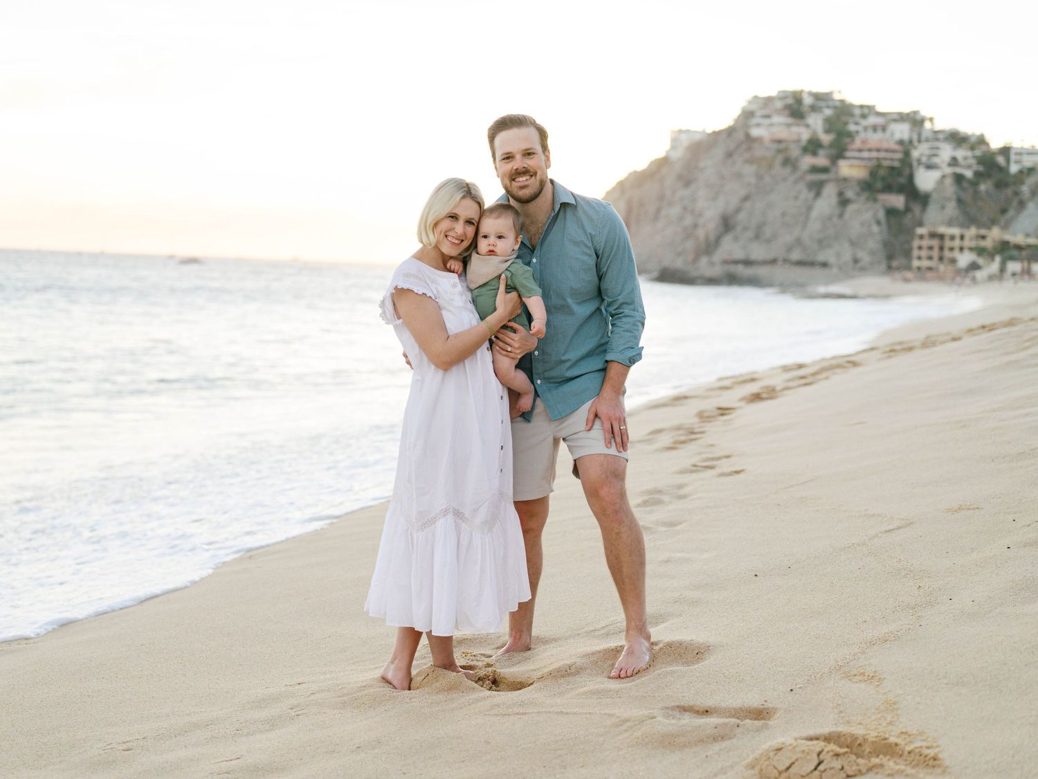 A family enjoys a sunset moment together on a sandy beach with cliffs in the background.