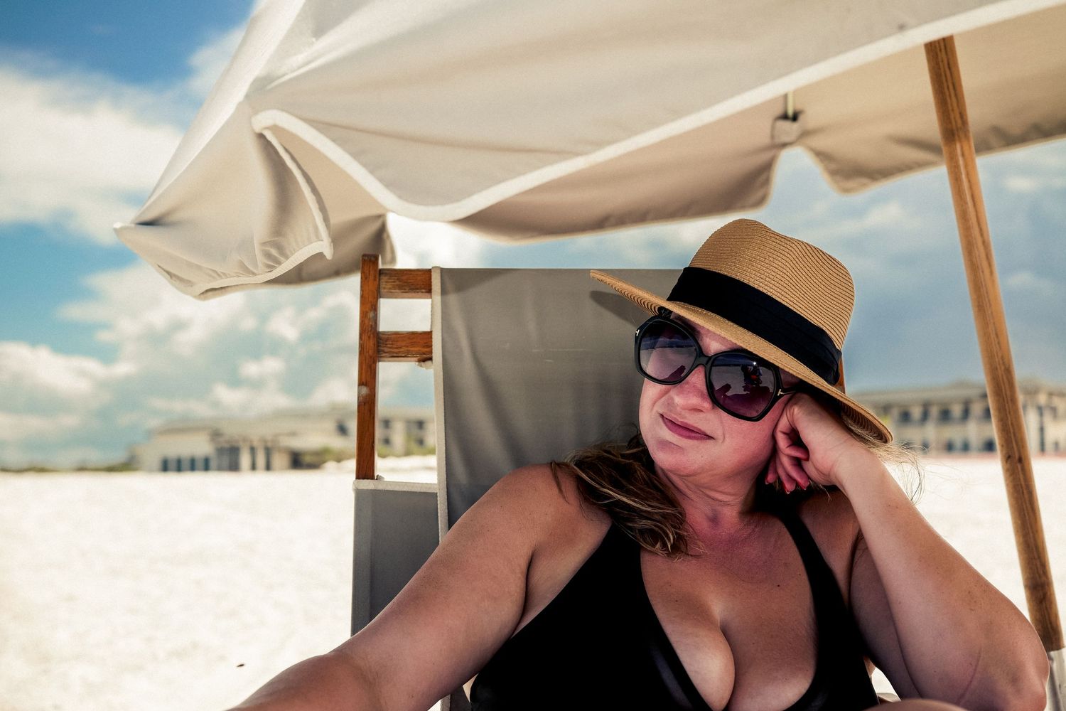Relaxing under a beach umbrella in a black swimsuit and straw hat on a white sand beach on a sunny day.