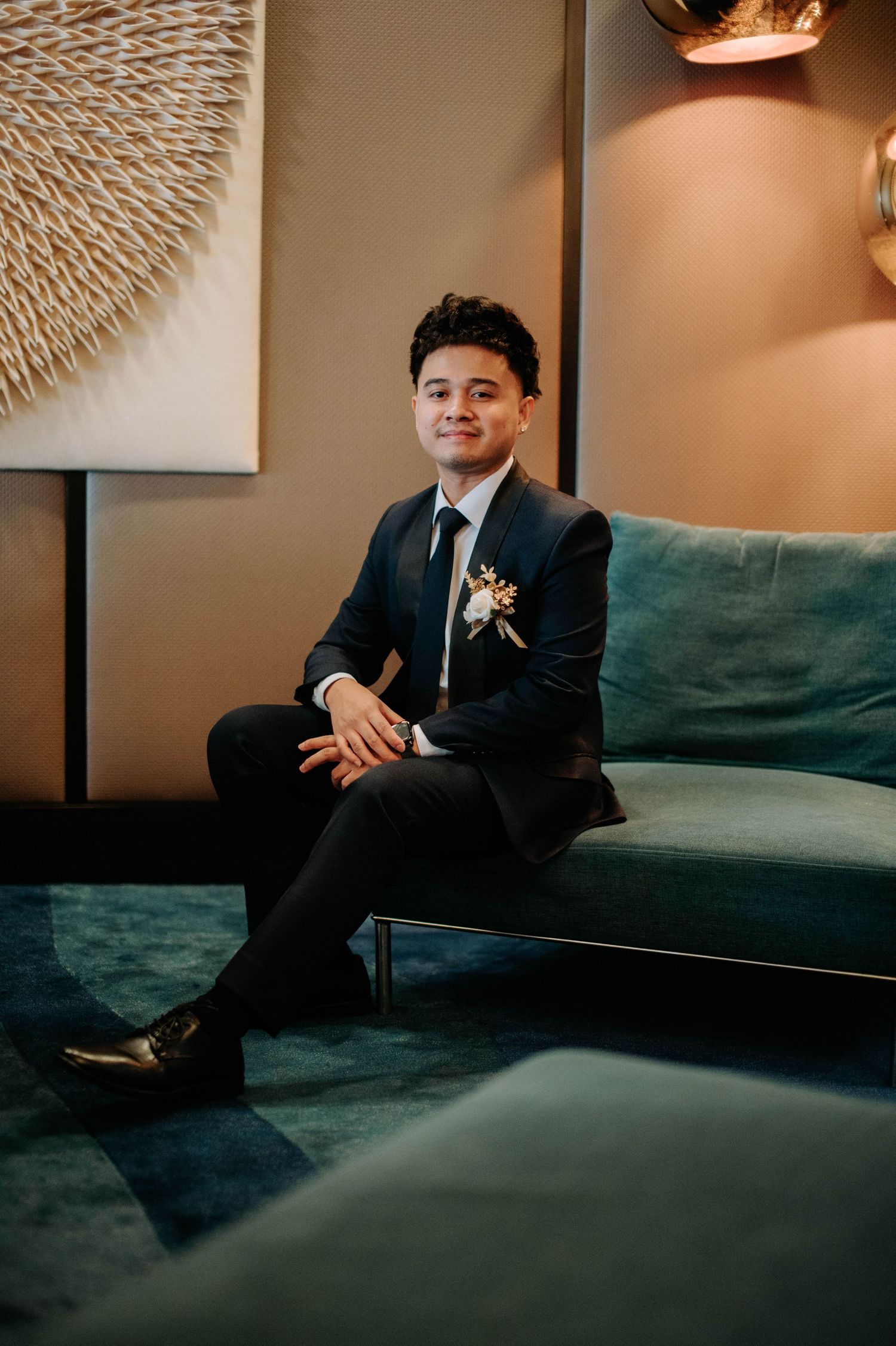 A formal portrait of someone seated on a teal velvet couch with modern decor.