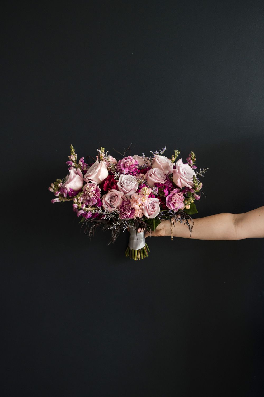 Elegant pink and mauve rose bouquet with delicate greenery held against dark background.
