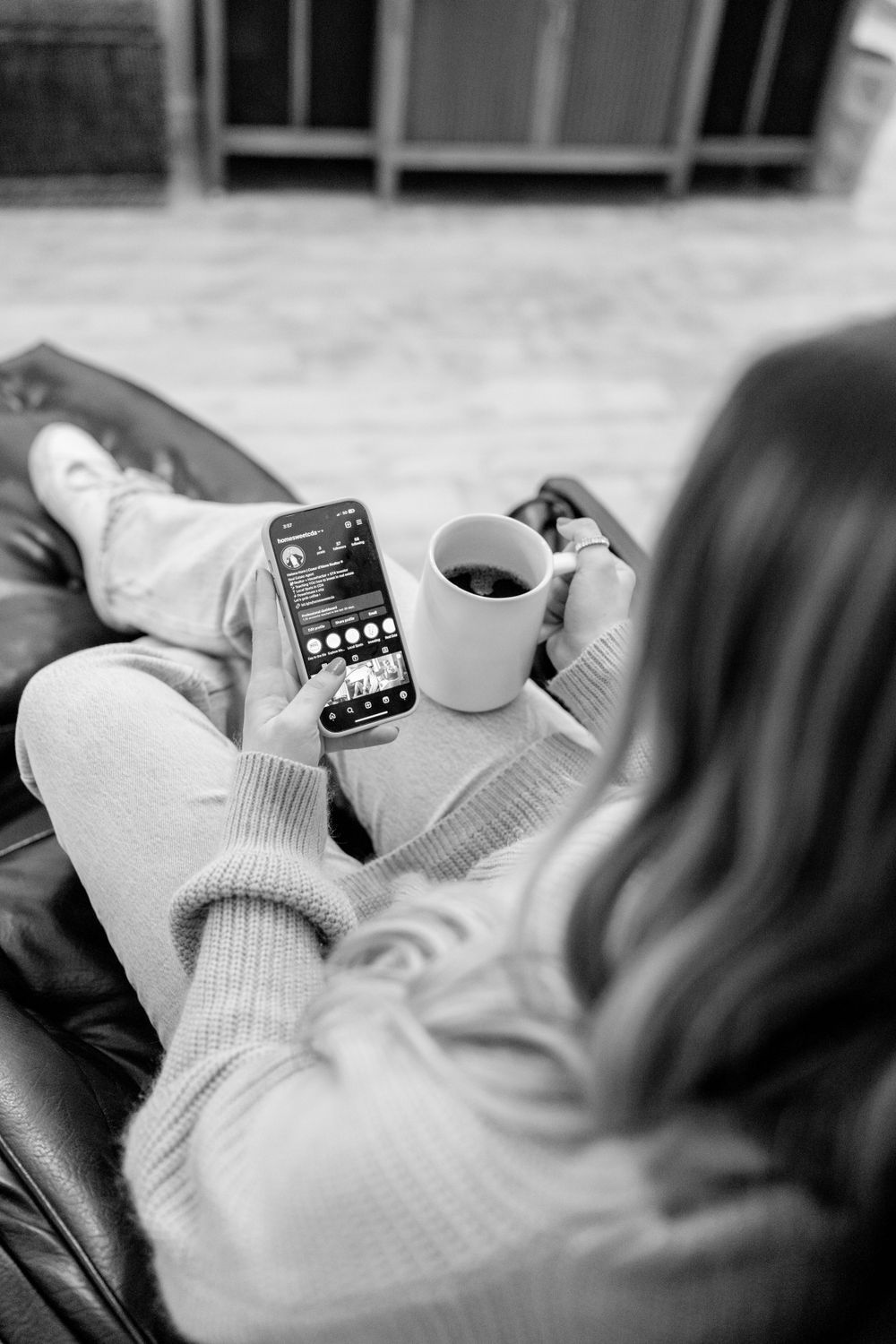 Person relaxing with coffee and phone on couch in black and white photography.