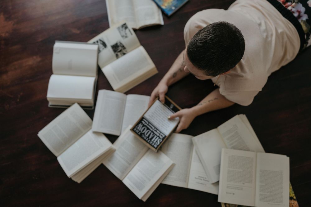 Overhead view of someone studying with multiple open books and notebooks spread out on a dark wooden surface.
