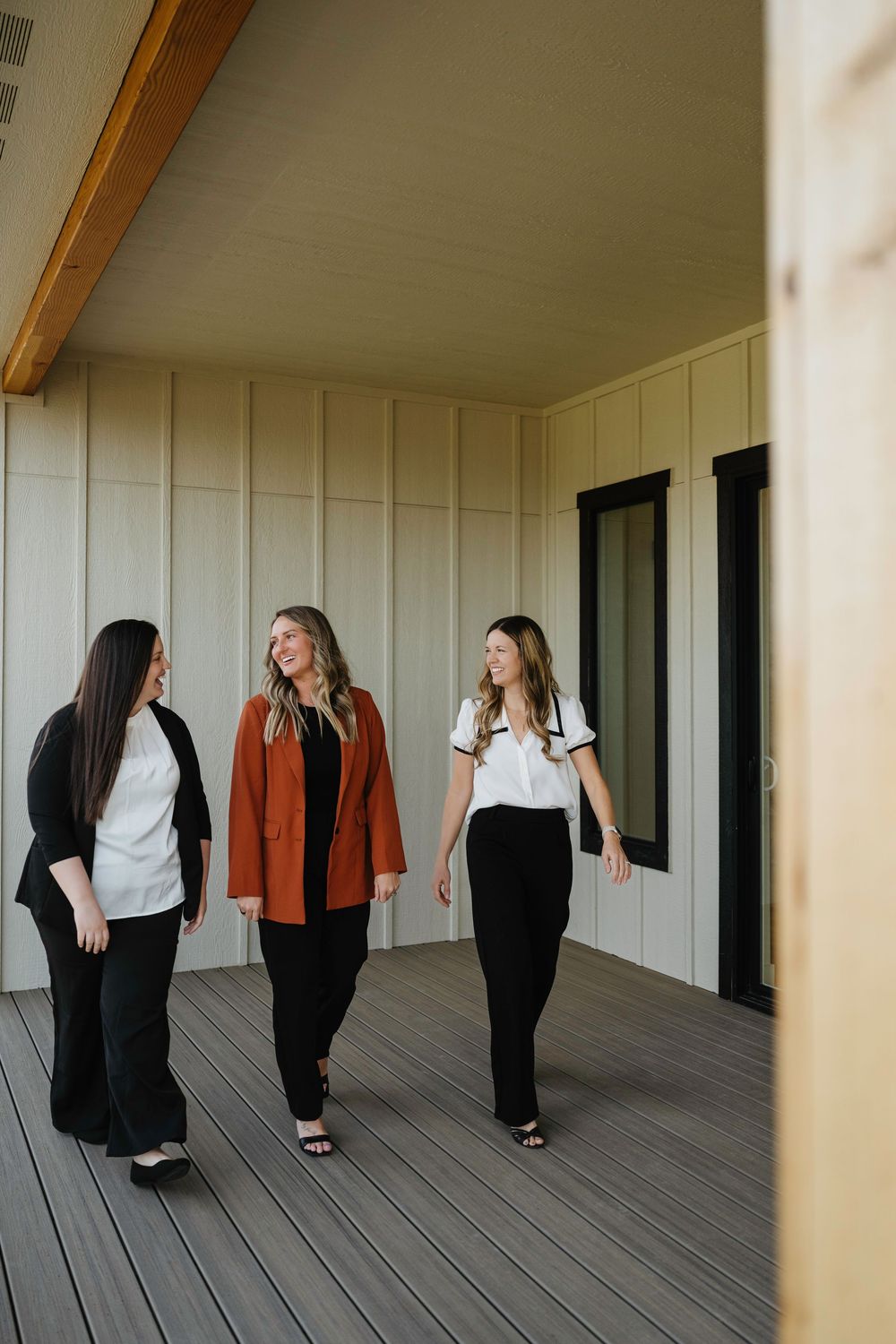 Three professional women walking and smiling on a modern building deck.