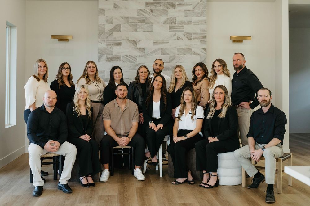 A professional real estate team poses for a group photo in a modern white interior with stone accent wall.