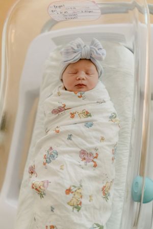 Newborn baby swaddled in floral print blanket resting in hospital bassinet.