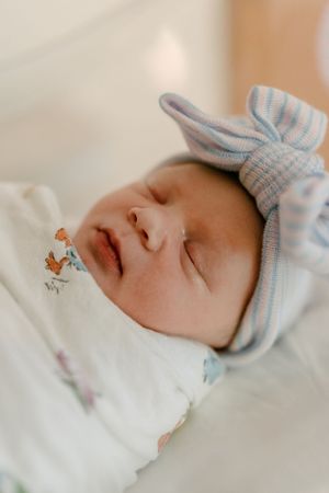 Close-up of peaceful newborn wearing striped blue bow hat and animal print swaddle.
