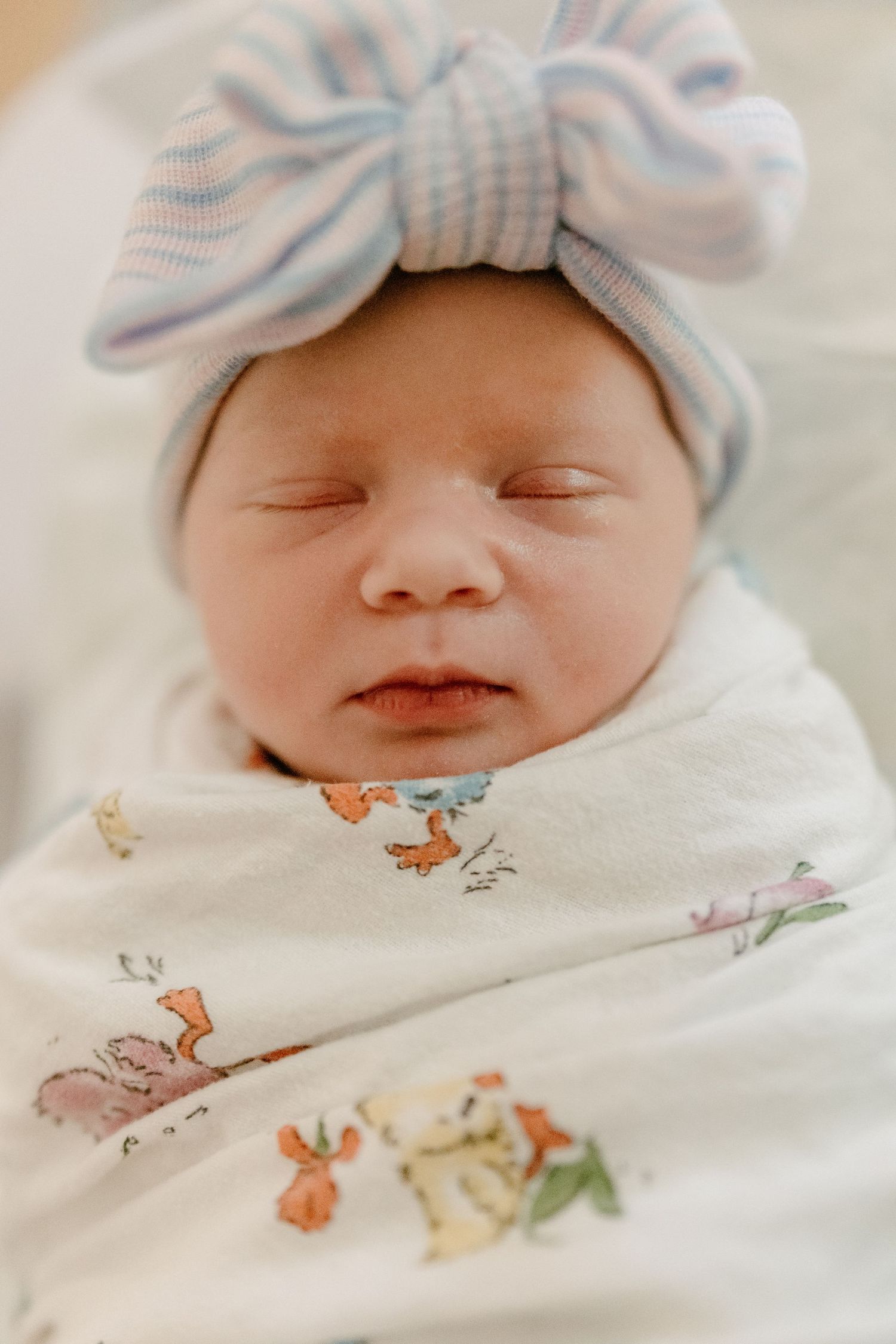 Sweet newborn baby resting in white swaddle with whimsical animal print and blue striped bow hat.