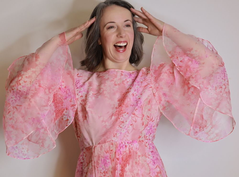 A joyful portrait in a vintage-style pink floral dress with dramatic bell sleeves.