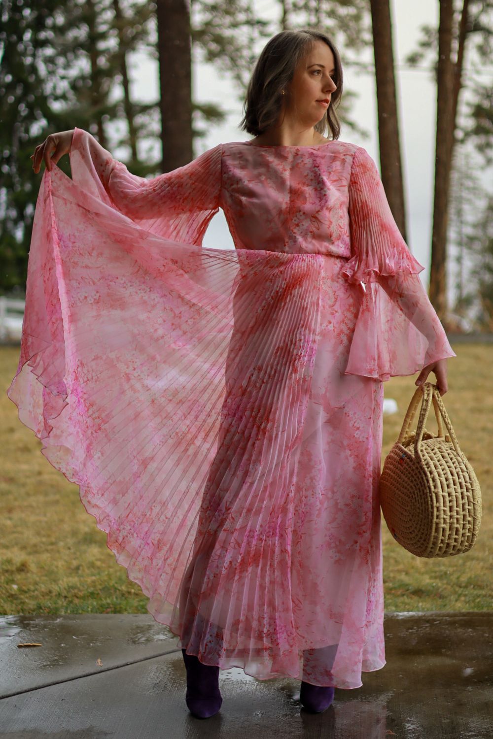 A flowing pink vintage dress being modeled outdoors with a woven basket.