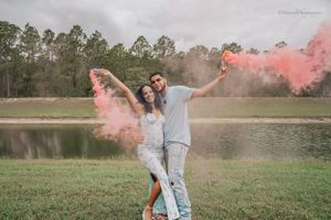 Couple poses playfully in an outdoor field with pink smoke bombs creating a dreamy atmosphere.